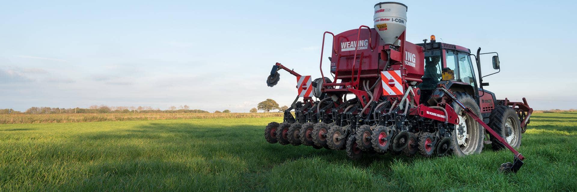 A large red agricultural vehicle being driven through a field of grass