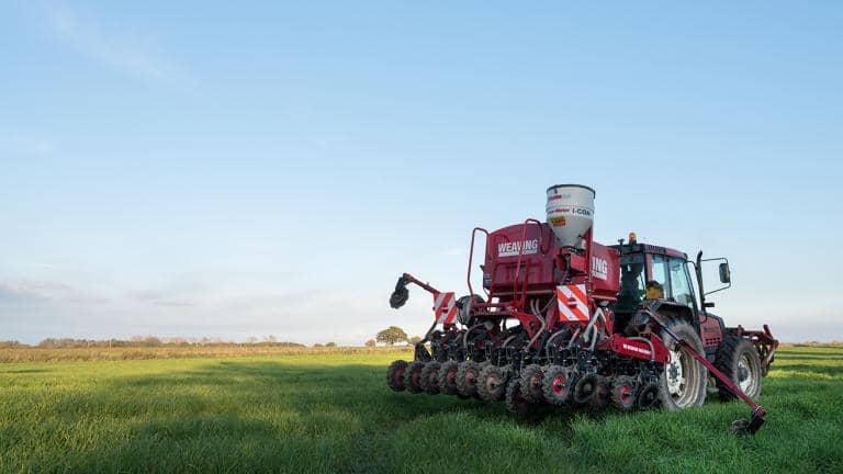 A large red agricultural vehicle being driven through a field of grass