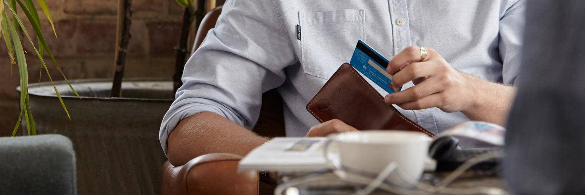 Close up of a man taking a blue bank card from a wallet 
