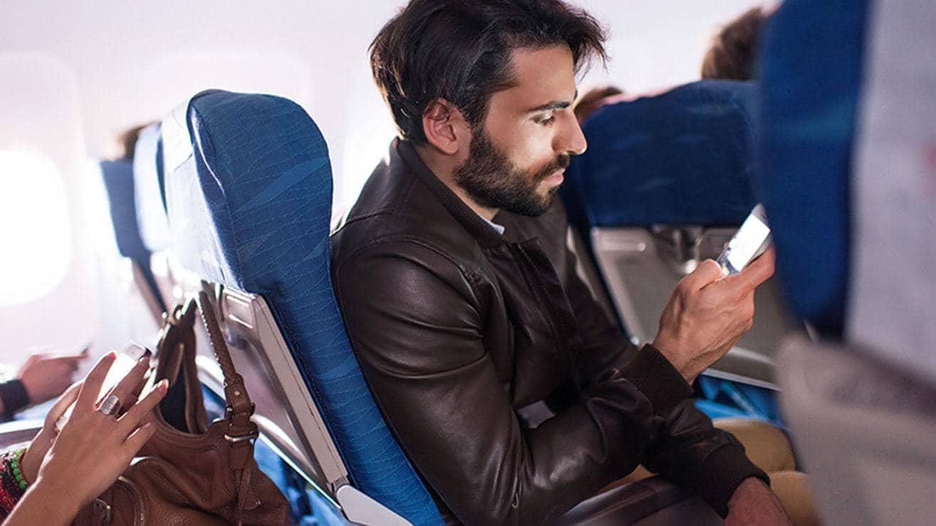A man sitting on a plane looks at his phone