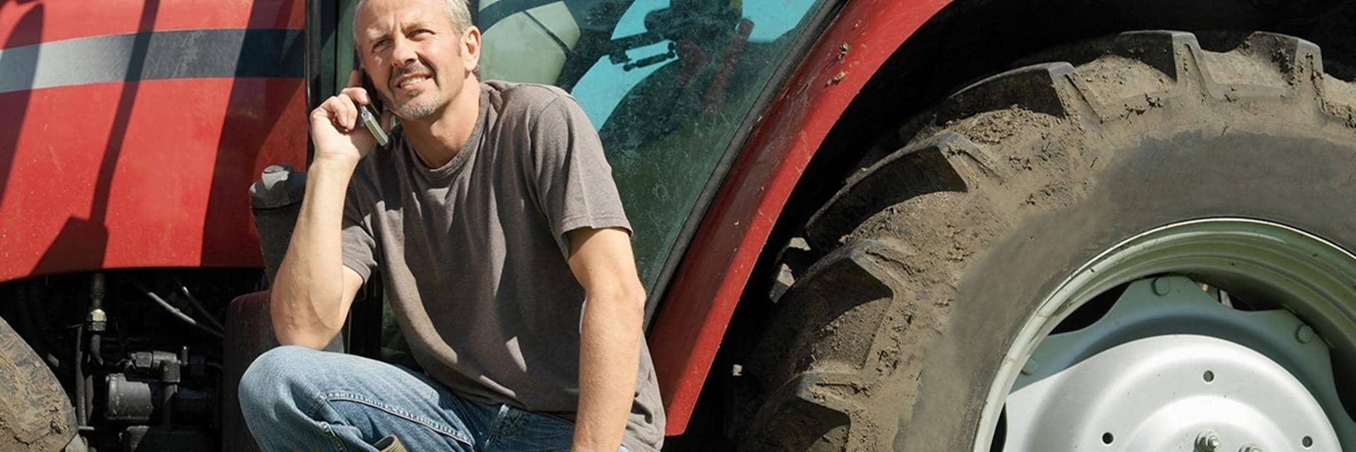 A farmer talks on his phone as he sits beside a muddy tractor