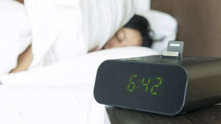 A person sleeping in bed. An alarm clock on the bedside table.