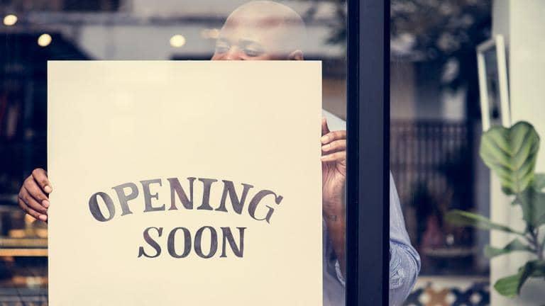 Man placing a hand written sign in a shop window which reads opening soon