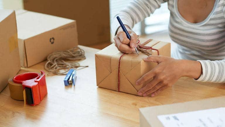 A woman writes an address on a hand wrapped brown paper parcel tied with string