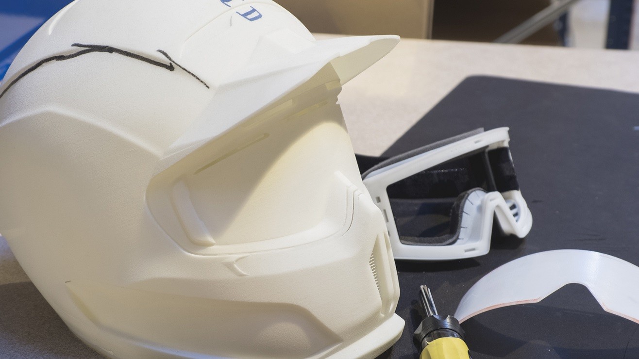 A prototype of a sports helmet beside a pair of ski goggles on a workbench