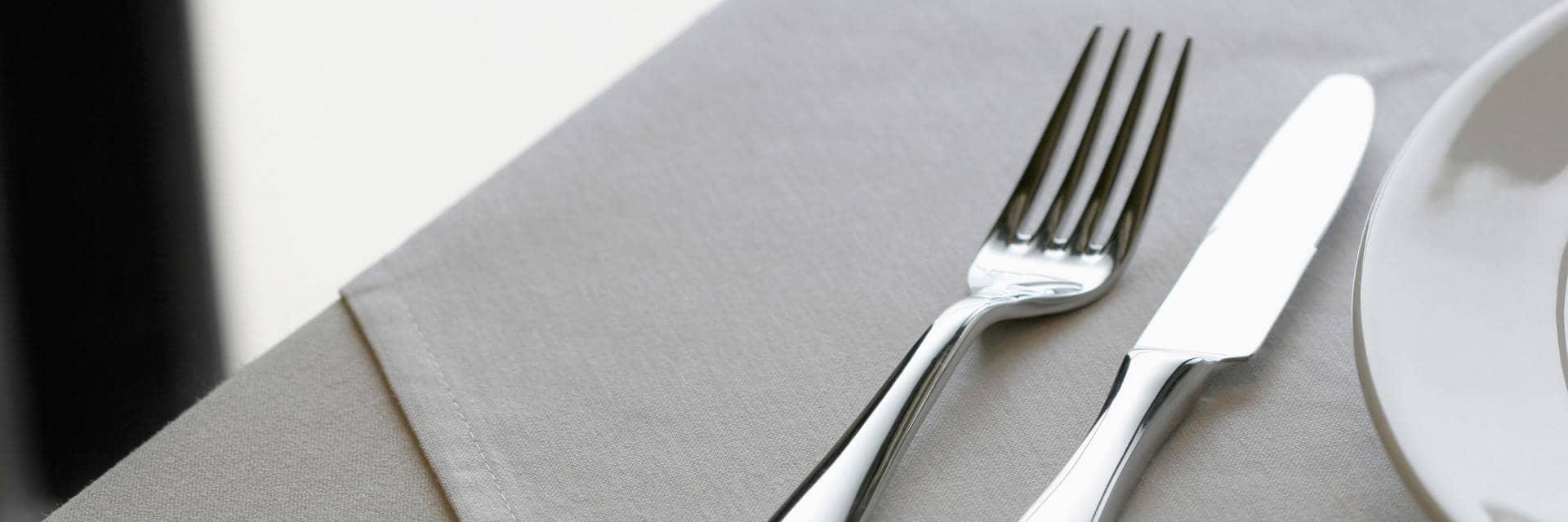  A knife and fork, and a side plate on top of a pale grey napkin