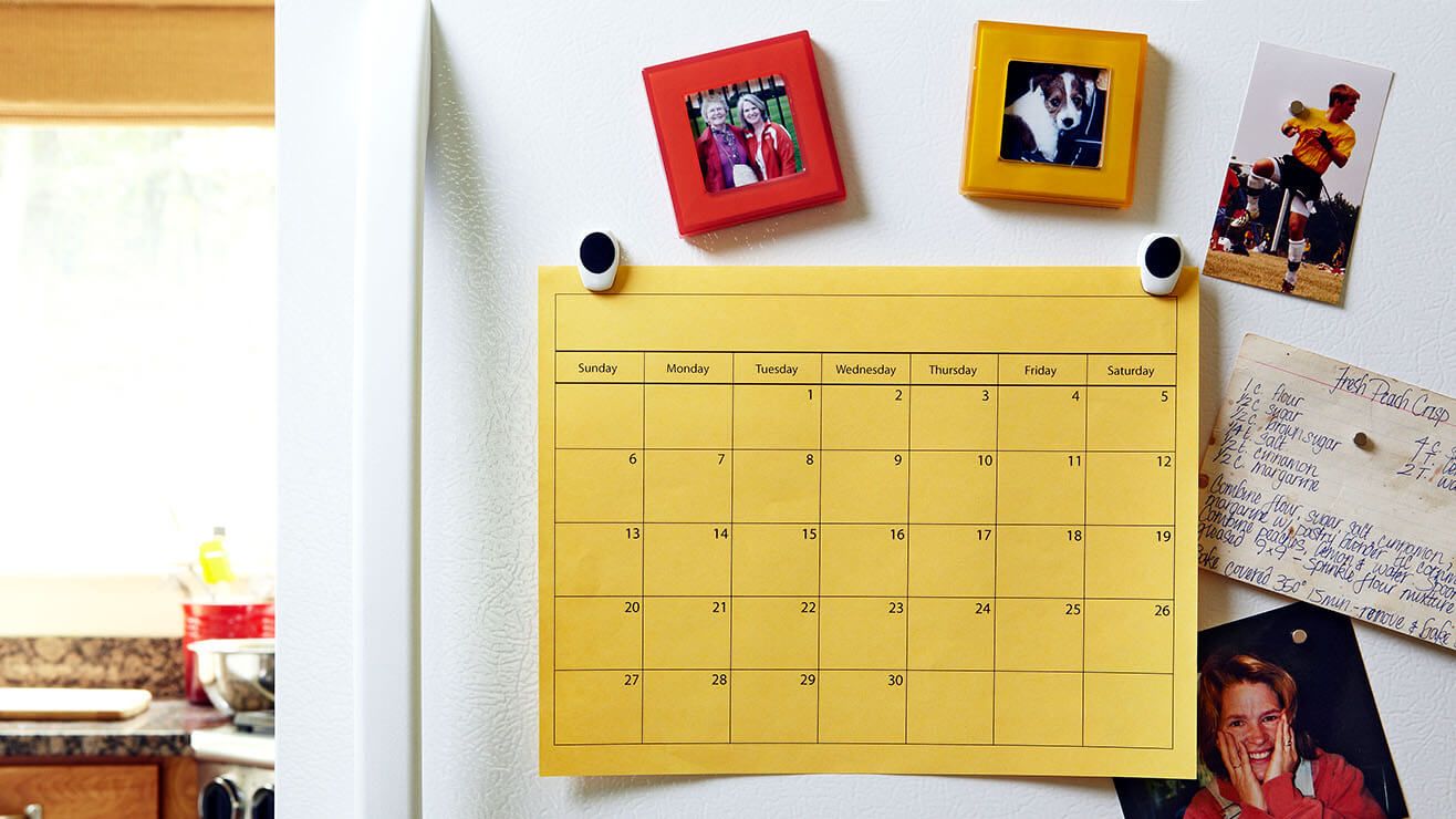 Calendar on a fridge door. It is held on with magnets and surrounded by family photos