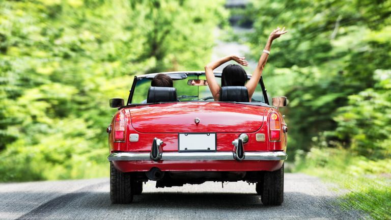 Couple driving through countryside in red soft top sports car