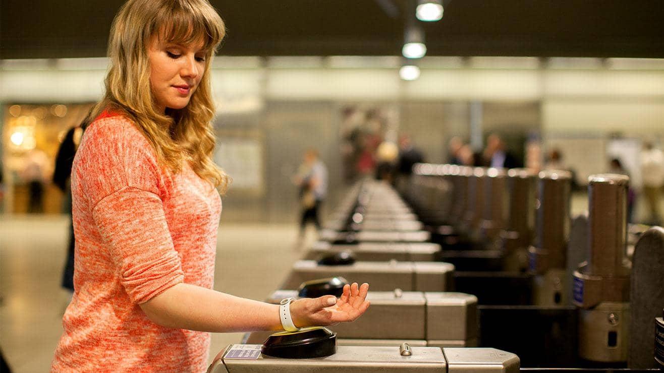 A woman taps her smart wristband against the card reader at the ticket barrier at a train station