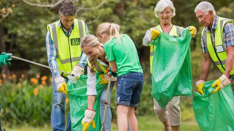  A group of people wearing gardening gloves pick up litter and put it in green bags
