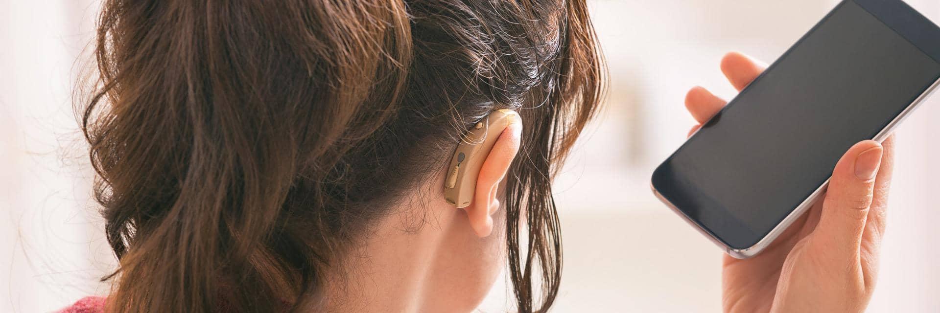  A woman wearing a hearing aid holds her phone near to her ear
