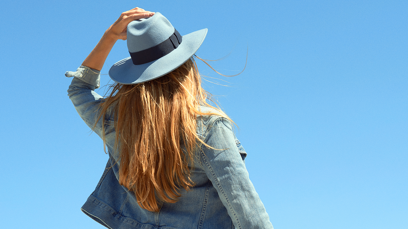 A woman wearing a hat looks up at a clear blue sky