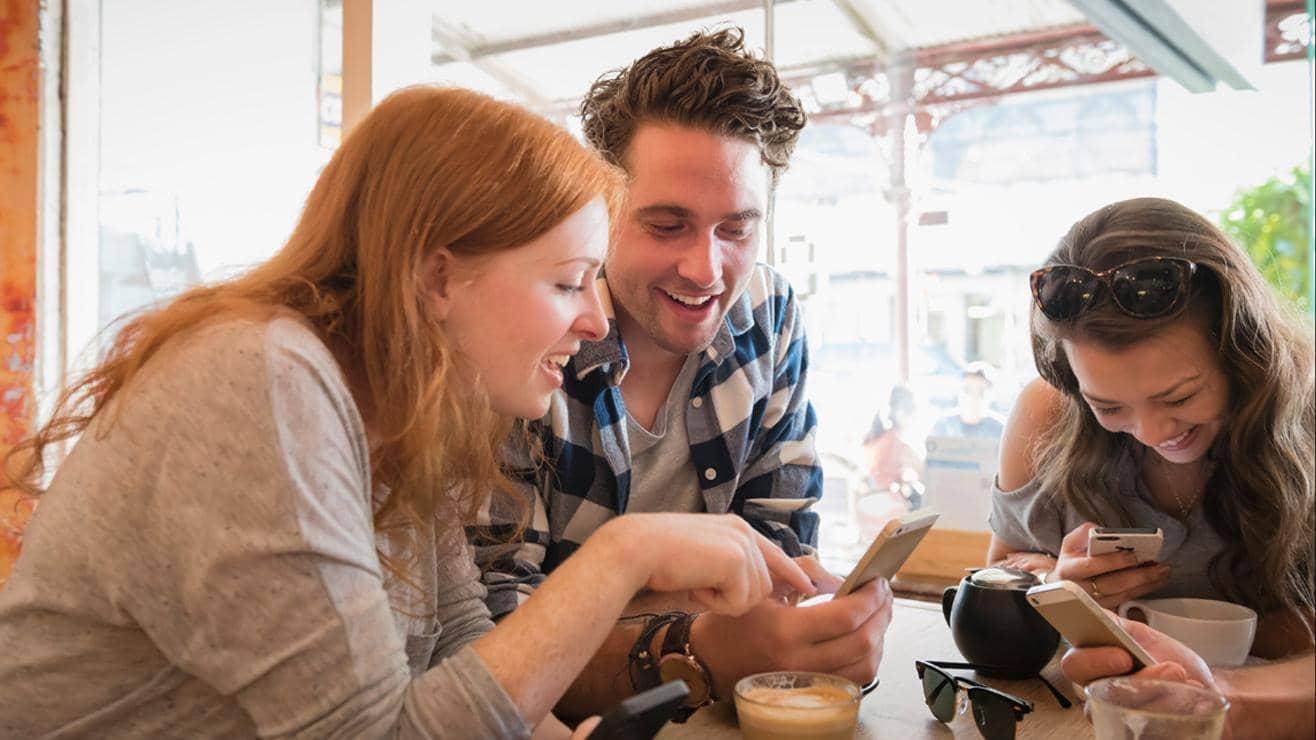 Three friends sitting around a table laughing as they look at their phones