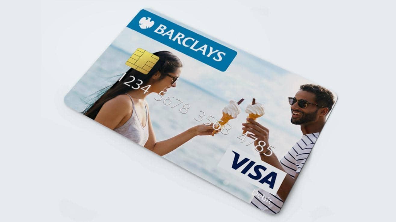 A man holding up a personalised Barclays card in front of a large picture showing the same image
