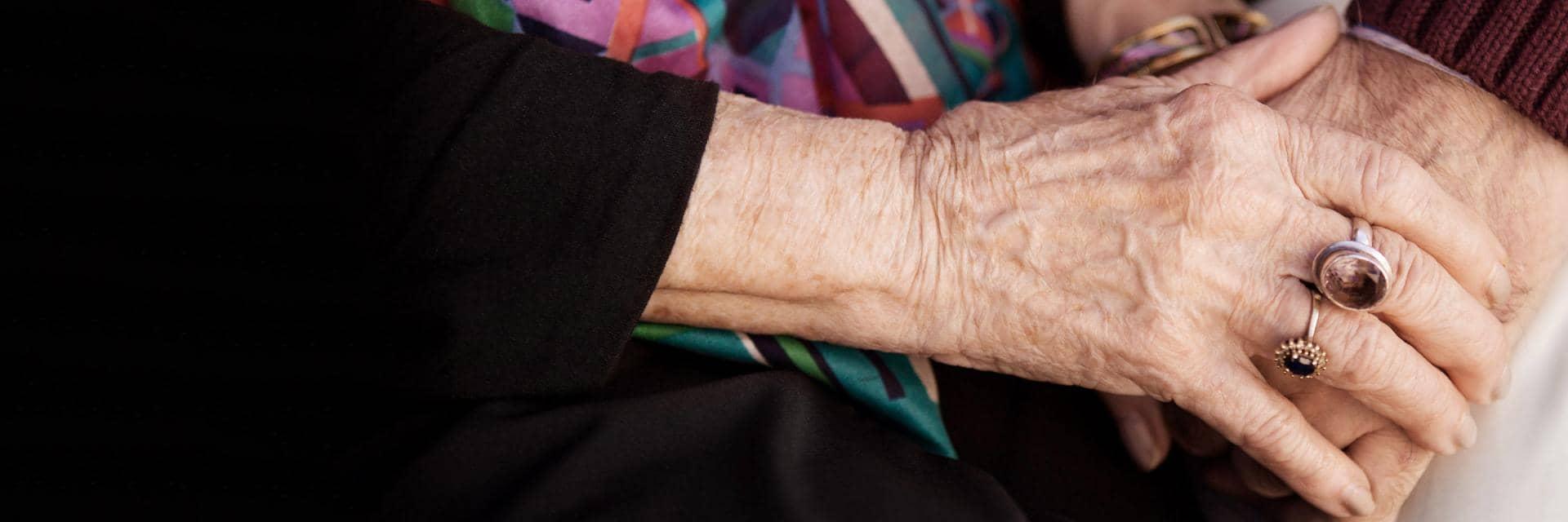  A person holds the hand of an elderly woman who is wearing rings on her fingers
