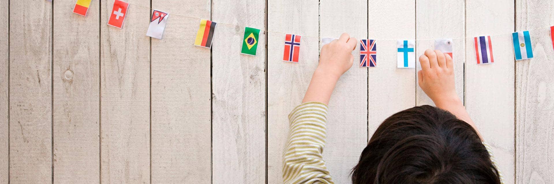  A child reaches up to touch a selection of national flags hanging on a piece of string against wooden cladding